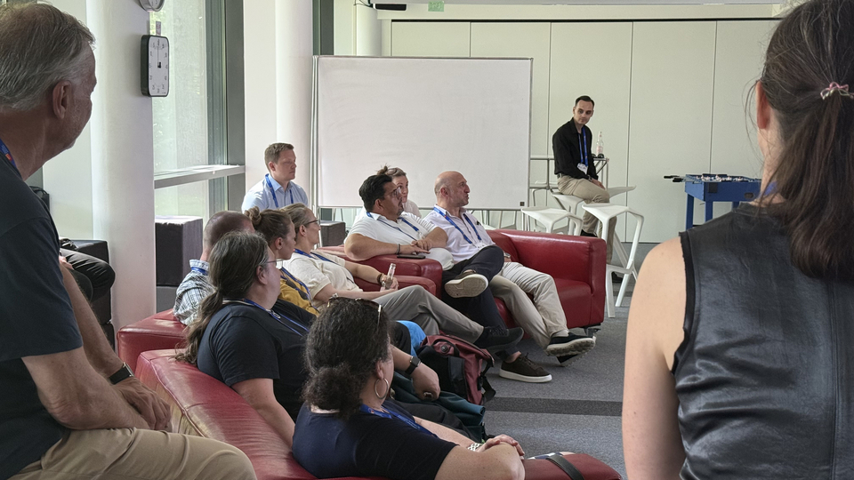 Gruppendiskussion in einem Konferenzbereich: Teilnehmende sitzen auf roten Sofas, während eine Moderatorin zur Runde spricht.