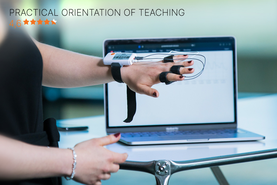 The picture shows the sensor-equipped hand of a student in front of a laptop. In the upper right corner of the picture is a purple seal of the current CHE Master's ranking. At the bottom of the image is a bar with the HPI's rating in the “Practical Orientation” category (4.6 out of 5 stars).