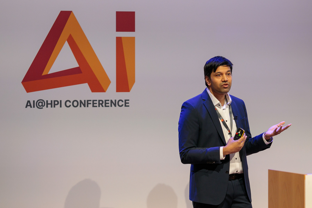 HPi-Professor Dr. Gerard de Melo hält einen Vortrag. Hinter ihm ist das Logo der AI@HPI Konferenz zu sehen.