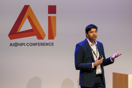 HPi-Professor Dr. Gerard de Melo hält einen Vortrag. Hinter ihm ist das Logo der AI@HPI Konferenz zu sehen.