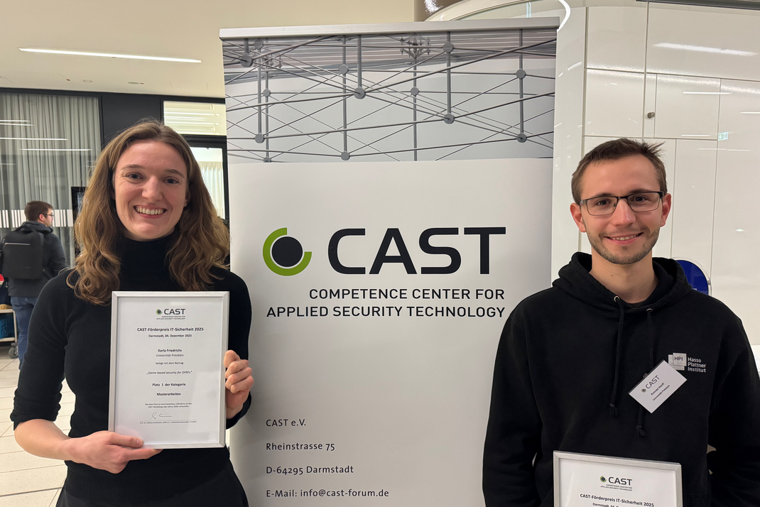 Die beiden HPI-Masterabsolvent:innen Karla Friedrichs und Konrad Hanff halten ihre Urkunden in den Händen. Im Hintergrund ist ein Banner des CAST e.C