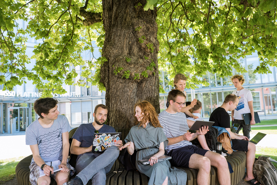 Studierende sitzen am Baum vor dem Hauptgebäude des HPI Campus I