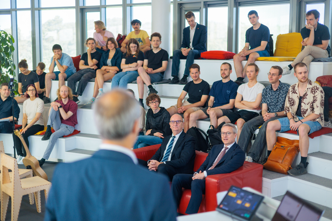 Brandenburgs Ministerpräsident Dr. Dietmar Woidke und Bundesdigitaminister Dr. Karsten Wildberger sitzen auf einem roten Sofa. Hinter ihnen sitzen Studierende des Hasso-Plattner-Instituts.