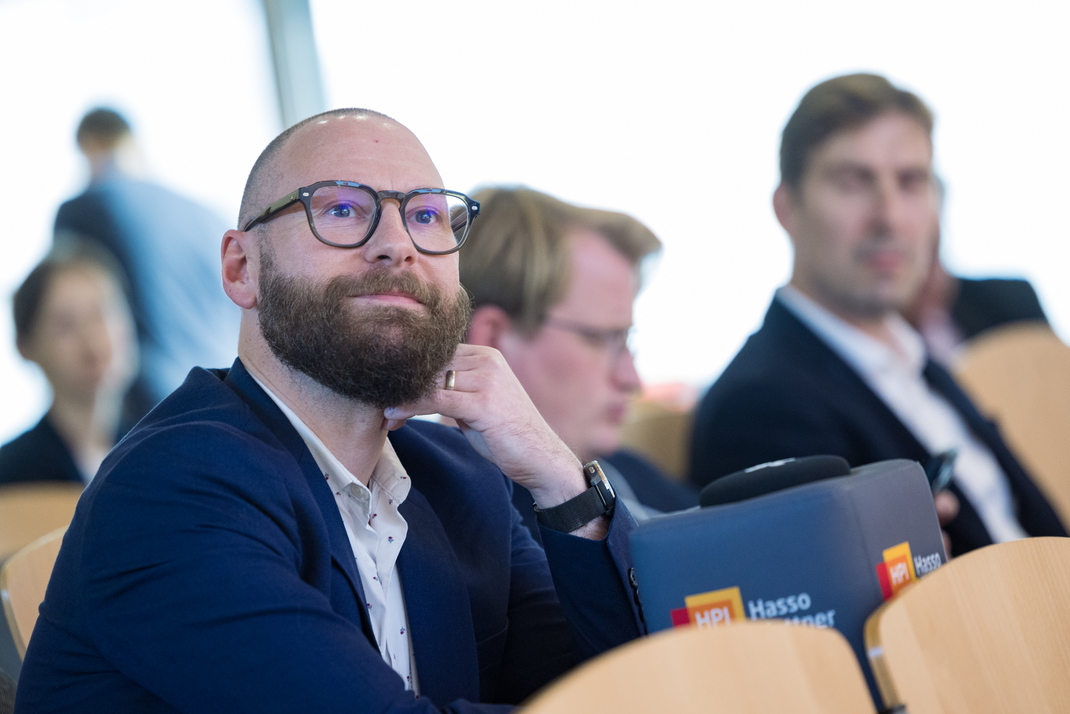 Teilnehmende der Clean-IT-Konferenz sitzen mit einem Mikrofon in Form eines großen HPI-Stoffwürfels im Plenum
