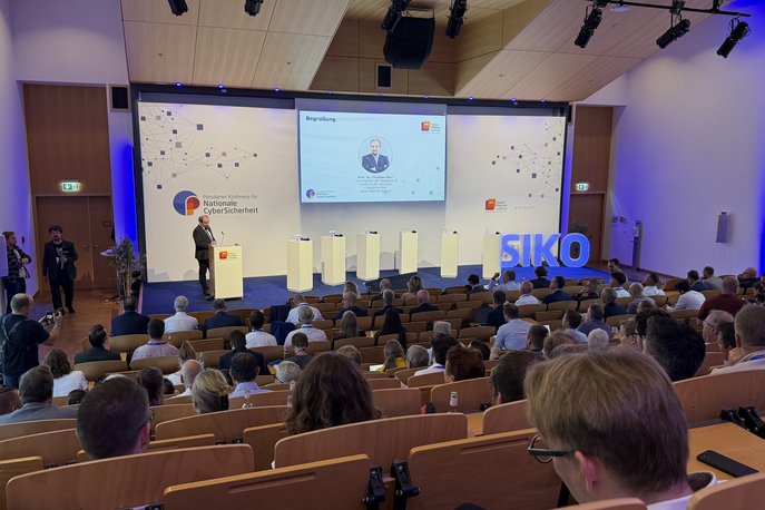 Weitwinkelaufnahme eines Konferenzhörsaals zur Begrüßung der Potsdamer Konferenz für Nationale CyberSicherheit, mit einem Redner am Pult und vielen Teilnehmenden im Saal.