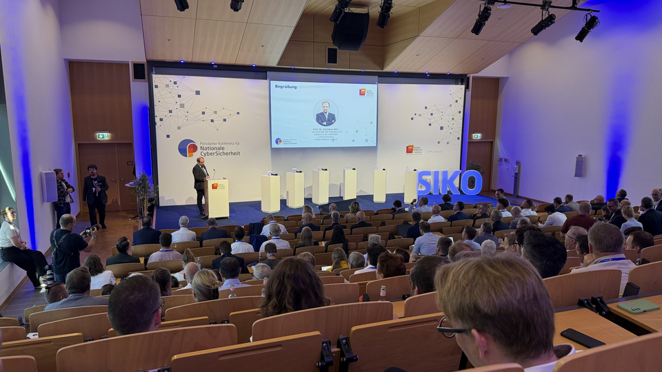 Weitwinkelaufnahme eines Konferenzhörsaals zur Begrüßung der Potsdamer Konferenz für Nationale CyberSicherheit, mit einem Redner am Pult und vielen Teilnehmenden im Saal.