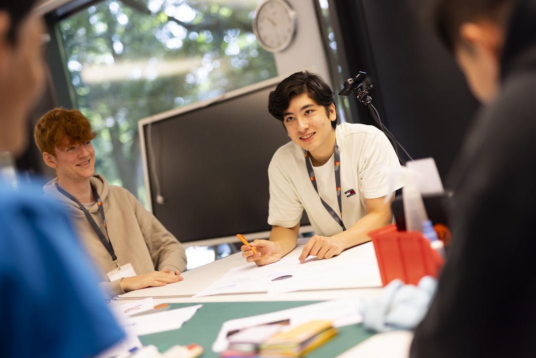 Teilnehmende des Sommercamps sitzen gemeinsam an einem Tisch und erarbeiten mit Stift und Papier ein gemeinsames Konzept