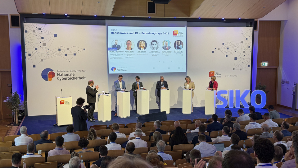 In einem großen Hörsaal findet eine Podiumsdiskussion zu Ransomware und KI bei der Potsdamer Konferenz für Nationale CyberSicherheit statt; auf der Bühne stehen mehrere Panelisten vor dem Publikum.