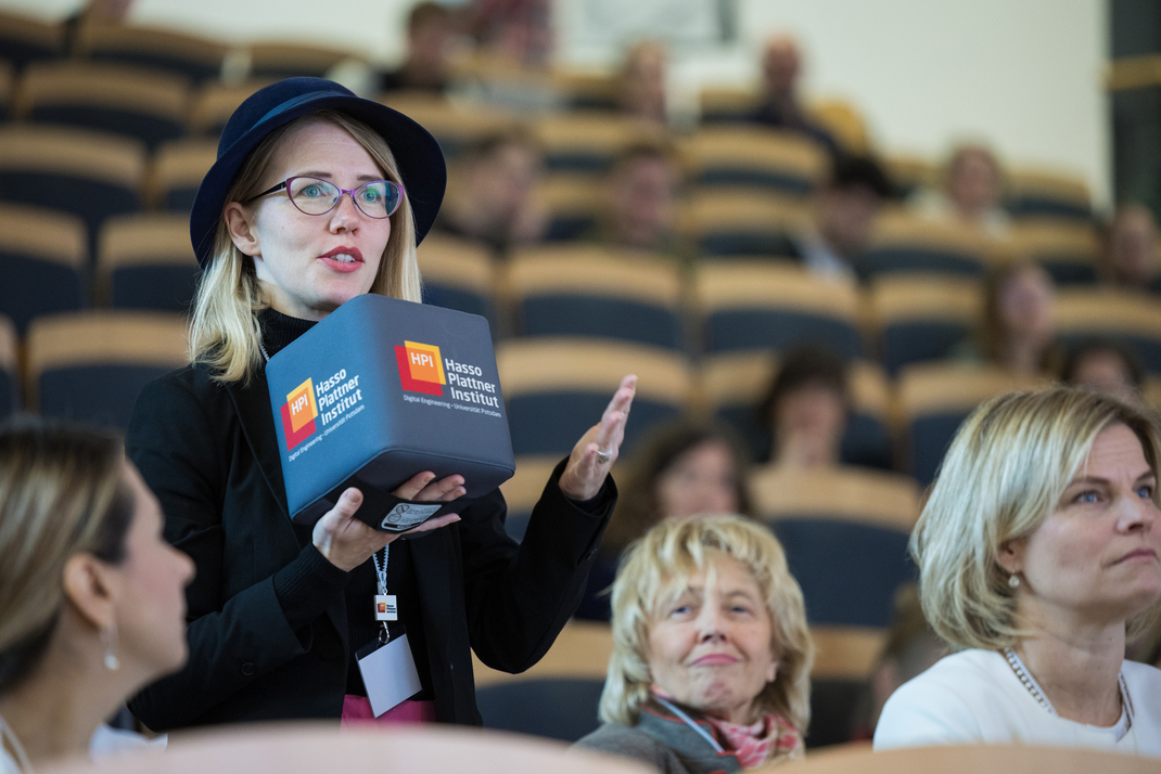 Aus dem Plenum heraus spricht eine Person mit einem Mikrofon in Form eines großen HPI-Stoffwürfels