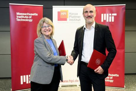 Sally Kornbluth and Tobias Friedrich shake hands. In the background are banners featuring the HPI and MIT logos.