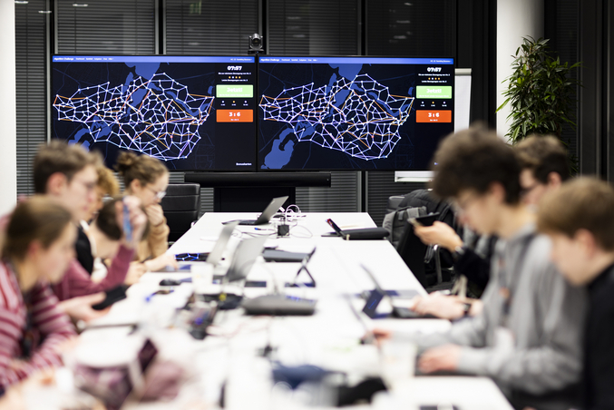 Teilnehmende des HPI BwInf-Camps arbeiten an ihren Projekten. Im Hintergrund zeigt ein Display Punktestände