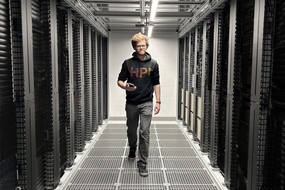 An AI expert walks towards us, smiling, passing through two rows of server racks.