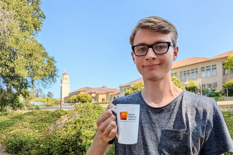 HPI-Bachelorstudent Valentin Teutschbein auf dem Campus der Stanford Universität mit einer HPI-Tasse in der Hand.