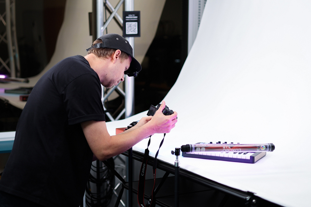 A person photographs a keyboard on a white background with studio equipment.