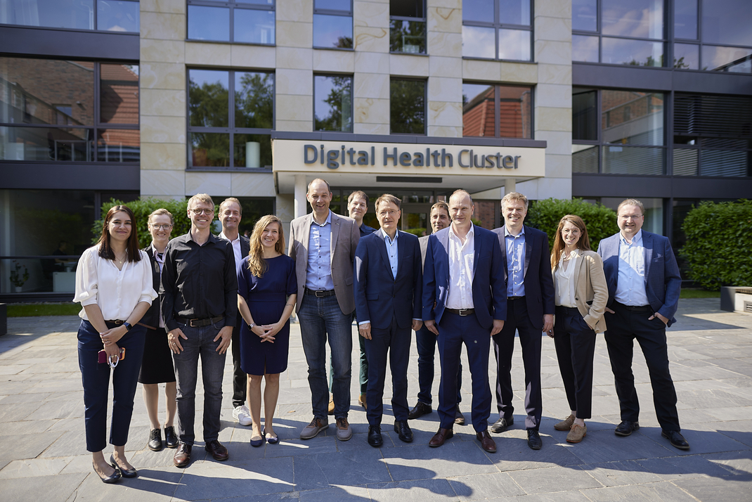 A group photo of Dr. Esther-Maria Antao, Prof. Katharina Baum, Prof. Christoph Lippert, Dr. Cornelius Remschmidt, Dr. Karina Oberheide, Prof. Ralf Herbrich, Dr. Stefan Konigorski, Prof. Karl Lauterbach, Dr. Matthieu Schapranow, Dr. Marcus Kölling, Prof. Bernhard Renard, Prof. Dr. Ariel Dora Stern, Prof. Bert Arnrich in front of the building of the Digital Health Cluster
