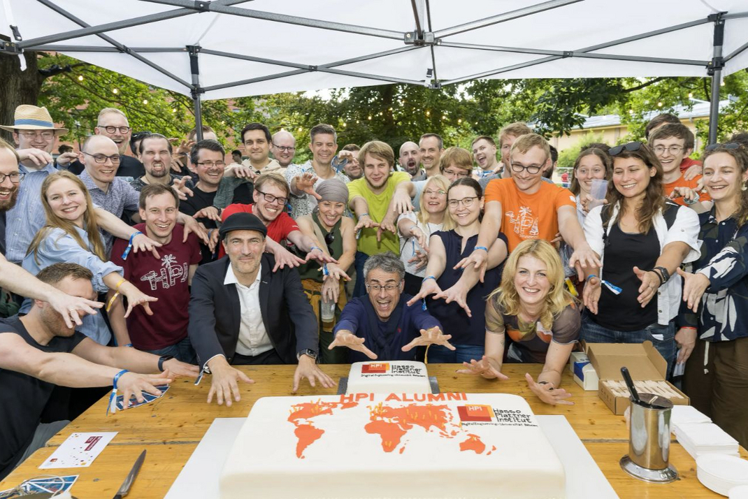 Alumni umringen einen Kuchen auf der HPI-Sommerparty. Die Torte ist mit einer orangefarbenen Weltkarte verziert.