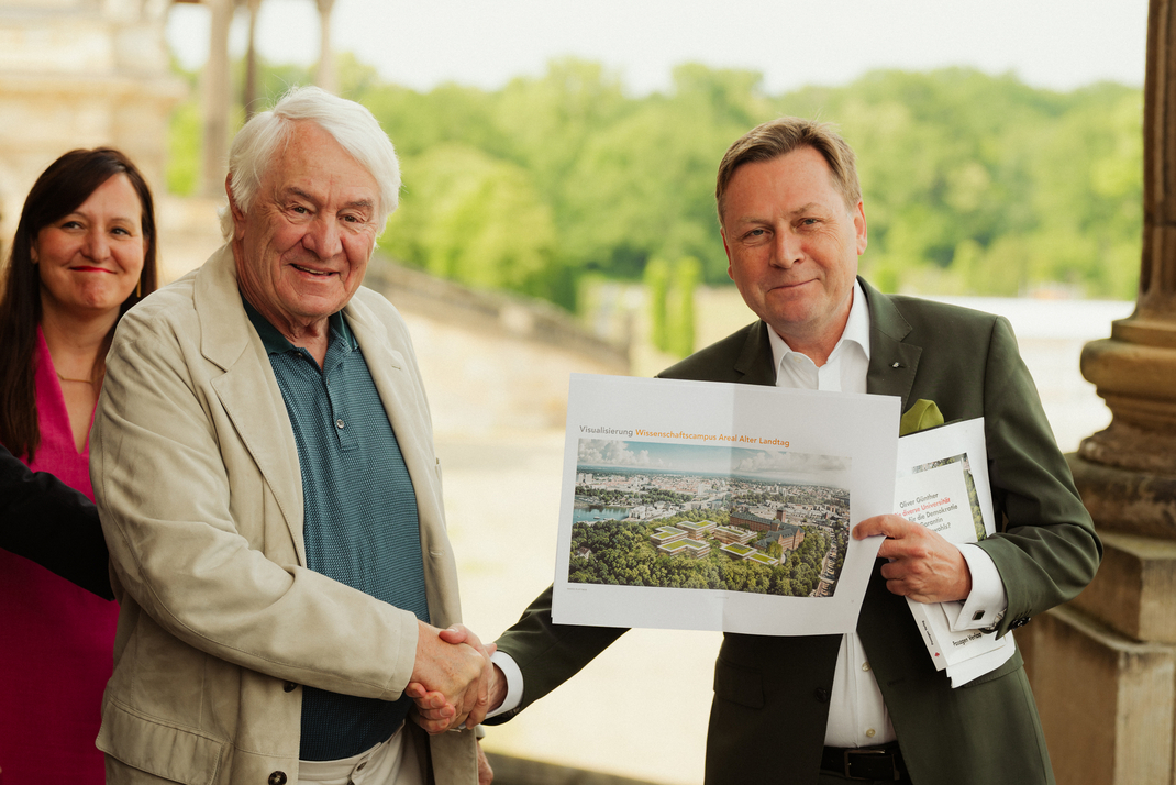Prof. Hasso Plattner, Gründer der Hasso Plattner Foundation (links) und Prof. Oliver Günther, Präsident der Universität Potsdam geben sich die Hand. Prof. Günther hält eine Visualisierung des zukünftigen Wissenschaftscampus in die Kamera. Im Hintergrund ist Dr. Manja Schüle, Ministerin für Wissenschaft, Forschung und Kultur des Landes Brandenburgs zu sehen.(Foto: Uni Potsdam/Kevin Ryl) 