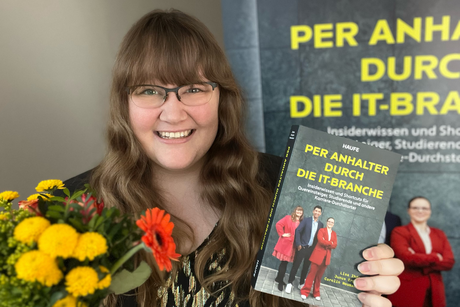 Lisa Ihde zeigt ihr Buch "Per Anhalter durch die IT" und hält einen Blumenstrauß in der Hand