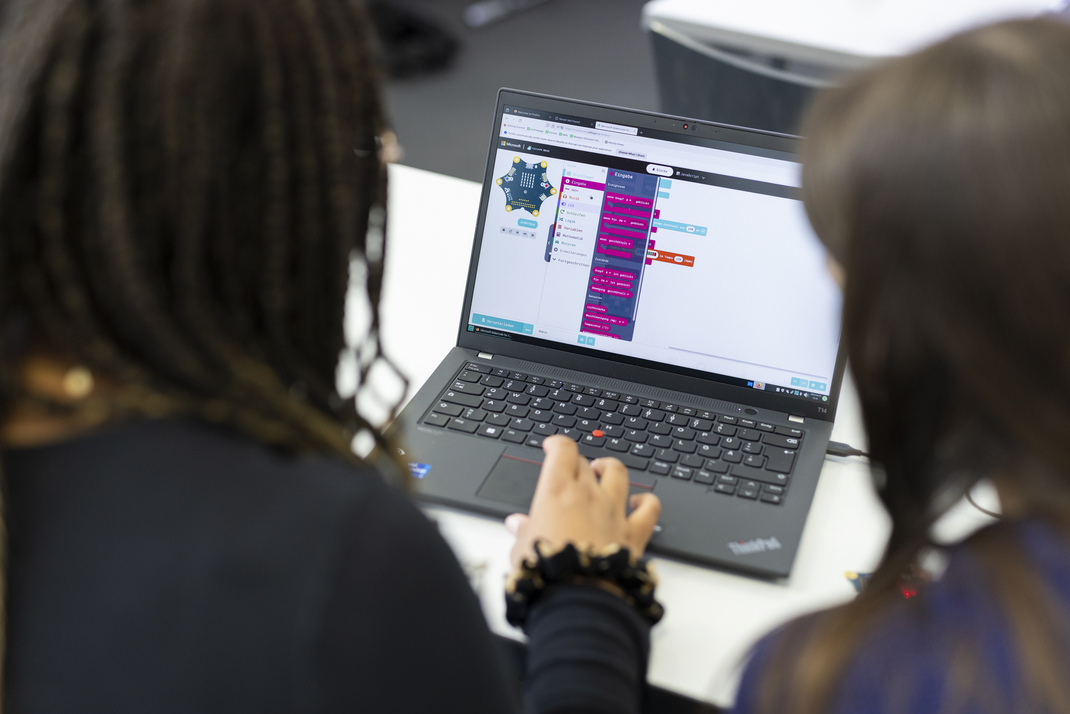 Zwei Teilnehmerinnen arbeiten gemeinsam an einem Laptop. Auf dem Desktop ist ein User-Interface zu sehen