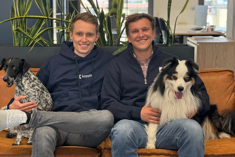 Die beiden koopla-Mitgründer Lasse Steffen (links) und Marco Trippler sitzen mit zwei Hunden auf einem Sofa in ihrem Büro. 