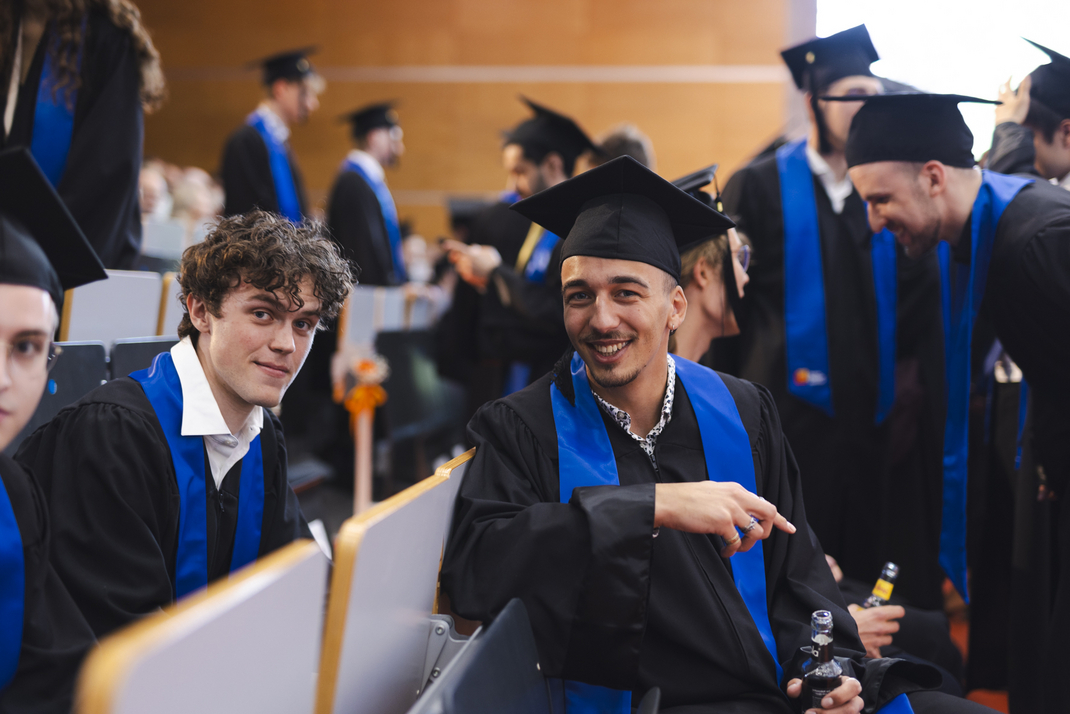 Graduates, dressed in their graduation gowns, are celebrating and chatting during the ceremony