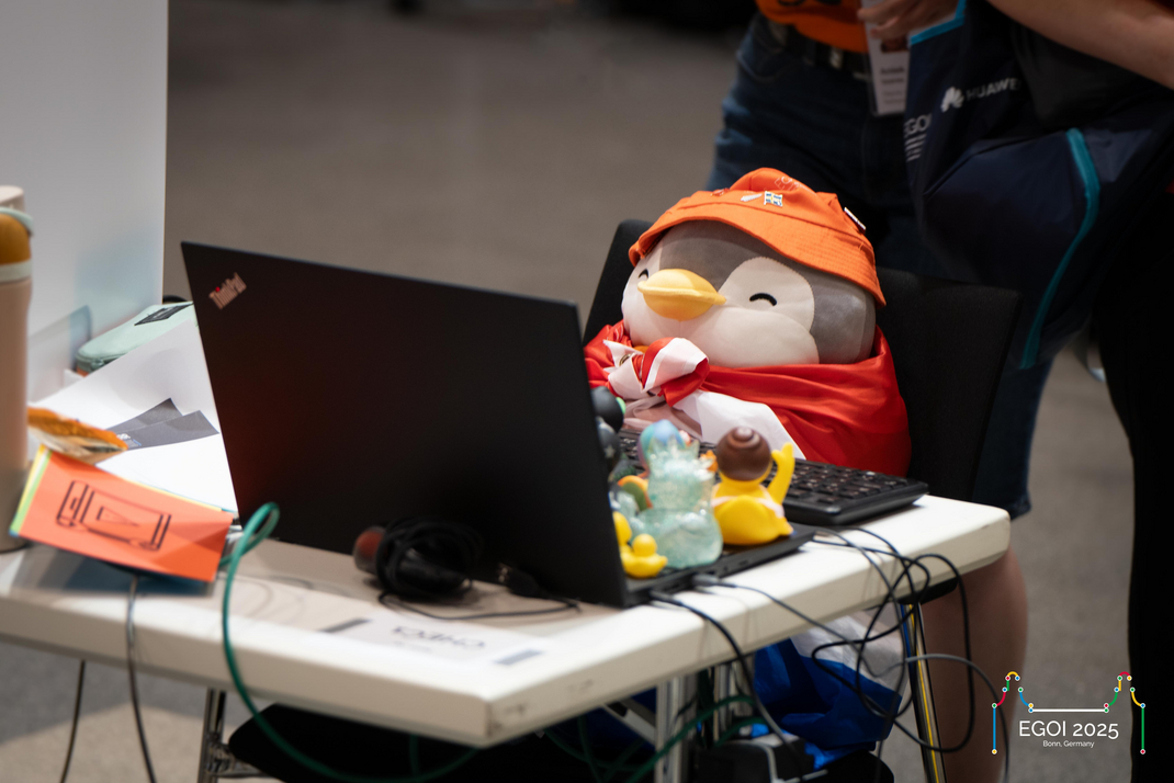 Ein Plüsch-Pinguin sitzt an an einem leeren Arbeitsplatz, als würde er an einem Laptop arbeiten. Auf dem Laptop sind verschiedene Gummi-Enten platziert.