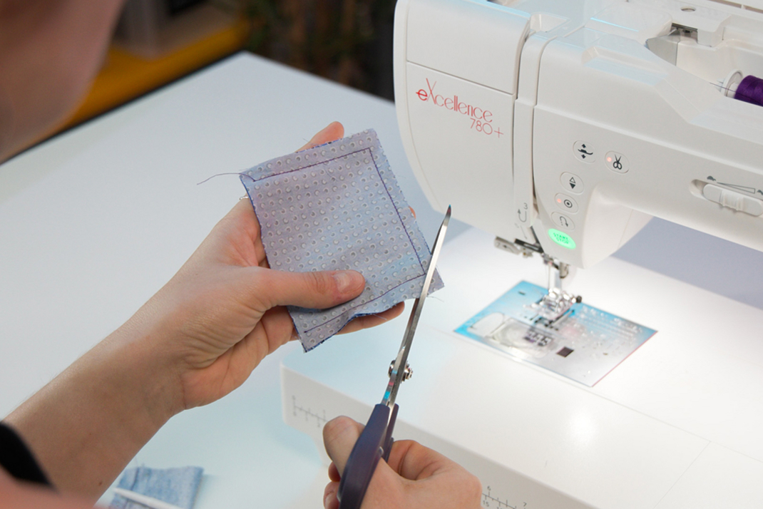 Someone is cutting something out of a piece of fabric. There is a sewing machine in the background.