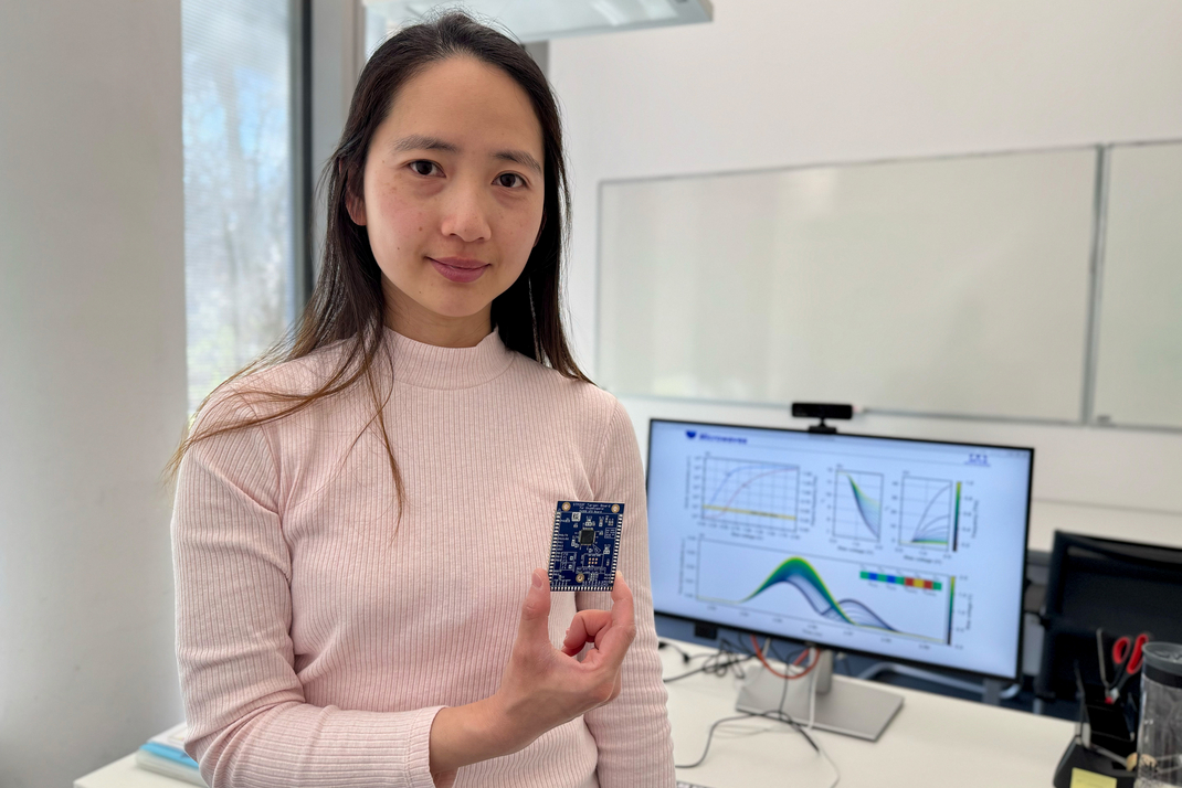 HPI professor Chitchanok Chuengsatiansup is standing in front of a desk with a computer monitor and holding a computer chip in her hand.
