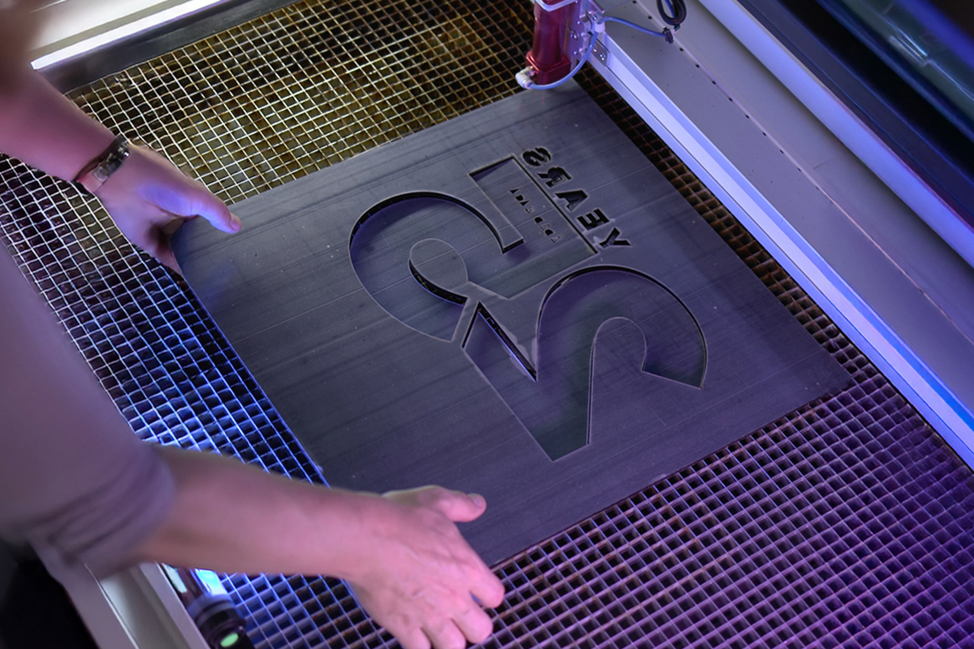 A 25-year HPI logo is cut out of a metal plate using a laser cutter.