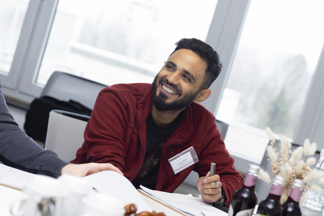 HPI master's student SaadBin is sitting at a conference table, smiling.