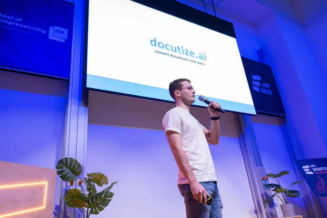 The startup team "Docutice.ai" is being presented on stage.