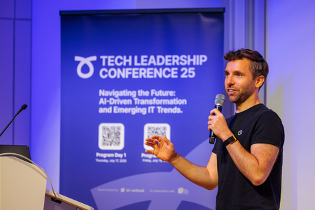 A speaker of the Tech Leadership Conference is talking into a microphone. In the background, a conference banner can be seen.