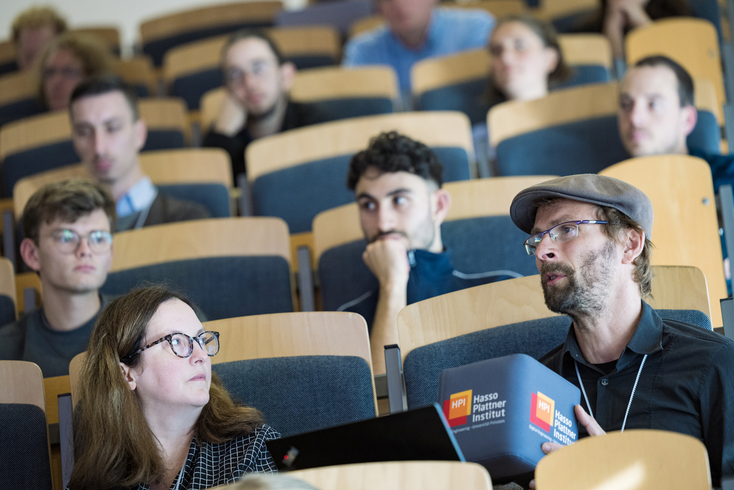 Teilnehmende der Clean-IT-Konferenz sitzen mit einem Mikrofon in Form eines großen HPI-Stoffwürfels im Plenum
