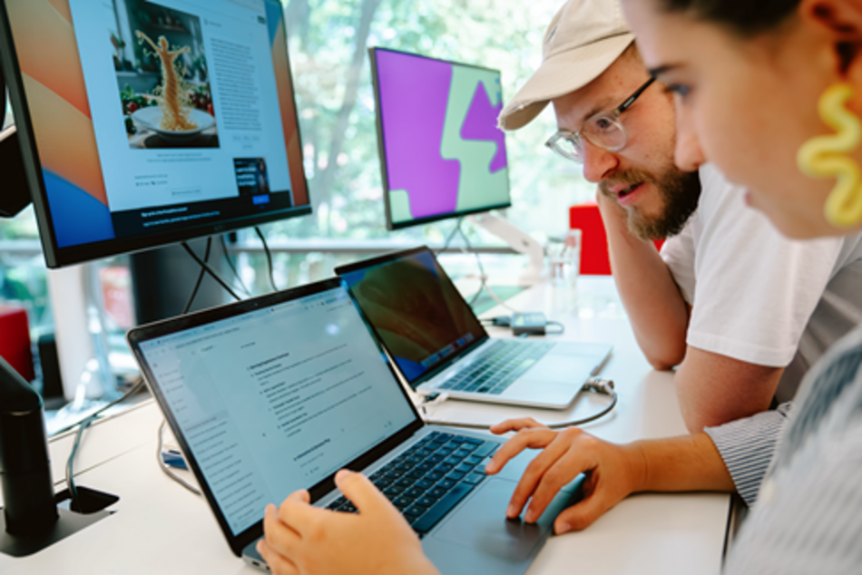Two participants in the HPI d–school Academic Programs are bent over a laptop, working together to design a website.