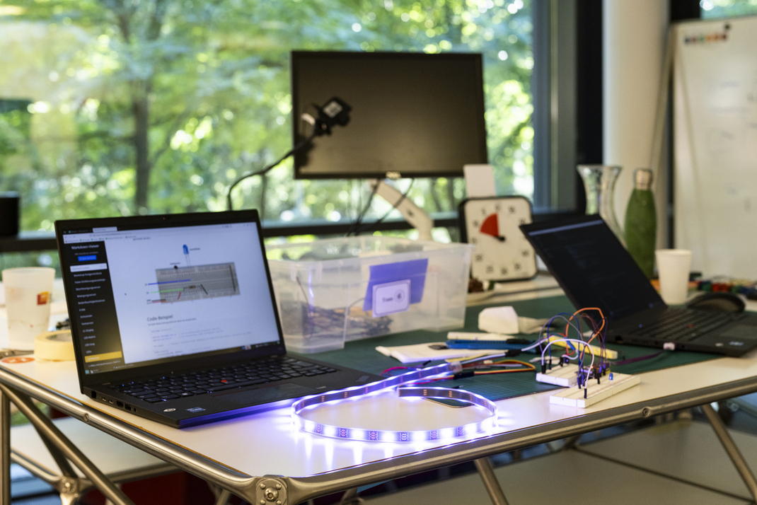 Ein leuchtender LED-Streifen ist mit Steckbrettern verbunden. Ein laptop zeigt eine Steckanleitung für die Konstruktion auf dem Tisch