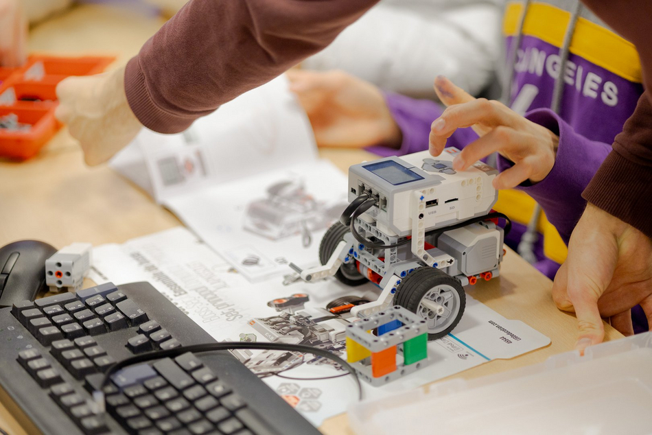 Nahaufnahme eines Roboters aus Lego-Technic. Der Roboter hat zwei große Räder und einen Computer mit Kabelanschlüssen, einem Display und Tasten zur Eingabe. 