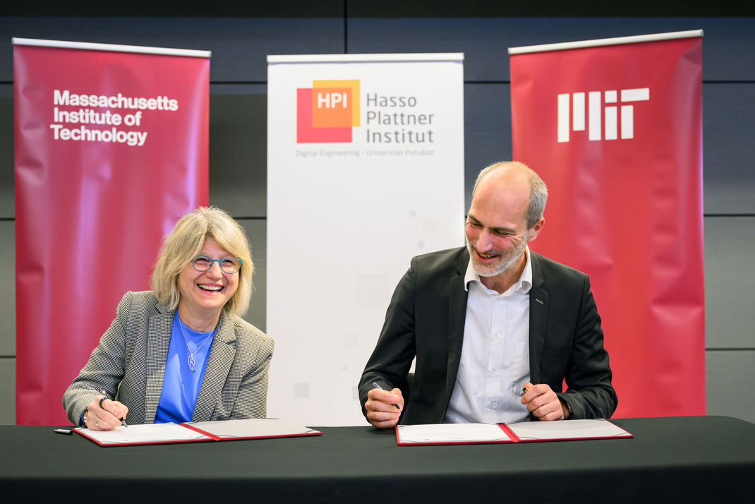 Sally Kornbluth and Tobias Friedrich each sign a document. In the background are banners featuring the HPI and MIT logos.