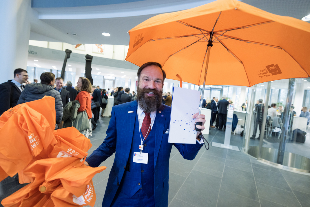 Ein Gast zeigt einen orangenen Regenschirm vom HPI