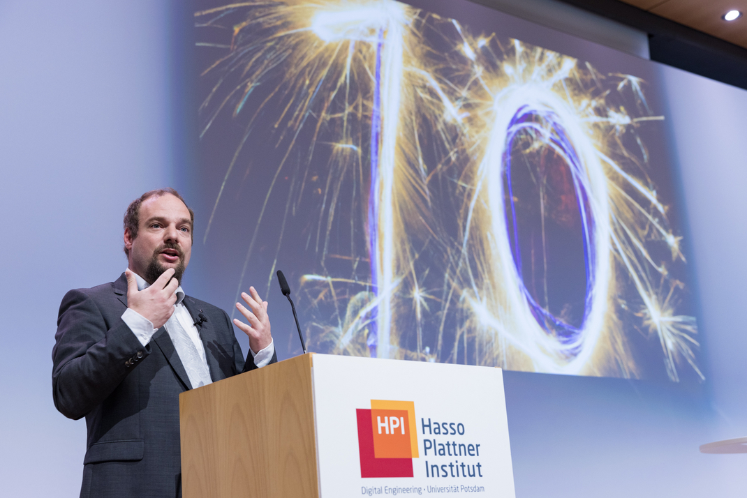 Prof. Dr. Christian Dörr begrüßt am Podium die Teilnehmer:innen der 10. Konferenz für Nationale Cybersicherheit. Hinter ihm ist das Bild einer aus Wunderkerzen geformten 10 zu sehen.