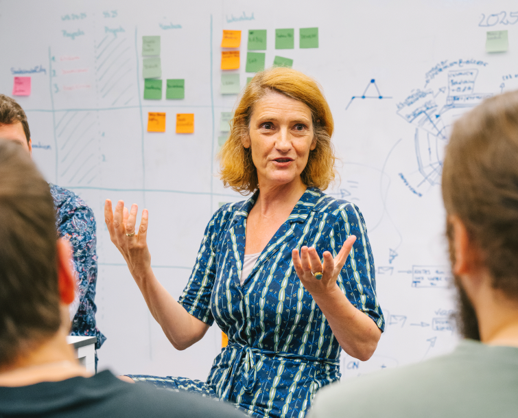 Several people are talking in front of a whiteboard with notes and Post-it notes on it. 